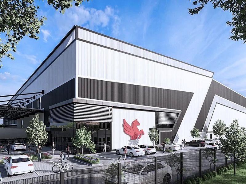 Modern industrial facility featuring large-scale metal cladding, a prominent loading bay canopy, and dedicated paved parking area within a secure fenced perimeter.