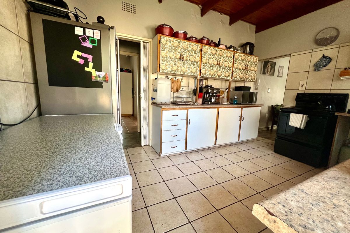 A functional kitchen featuring tiled flooring, exposed timber ceiling beams, and ample built-in cabinetry, offering potential for a modern renovation.