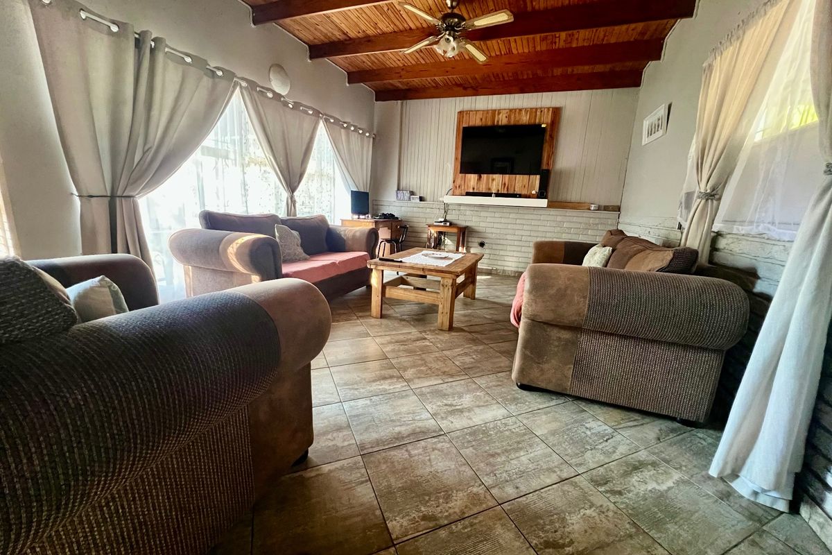 A cozy living room featuring a rustic exposed timber beam ceiling, tiled flooring, and a brick feature wall with integrated television mounting.