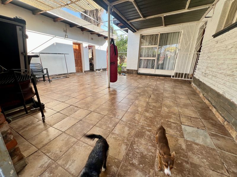 A covered outdoor patio area featuring tiled flooring, a sliding door entrance, and security gate access to the main dwelling.