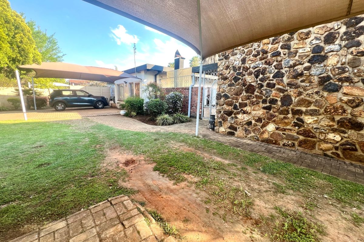 Rear garden area featuring stone-clad wall, paved pathways, and a large shade sail structure over the driveway.