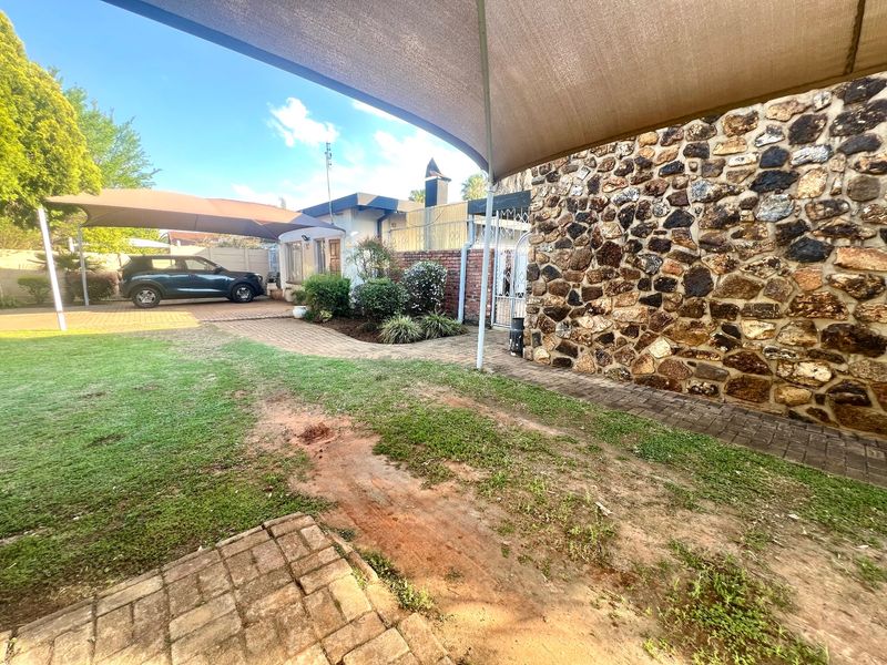 Rear garden area featuring stone-clad wall, paved pathways, and a large shade sail structure over the driveway.