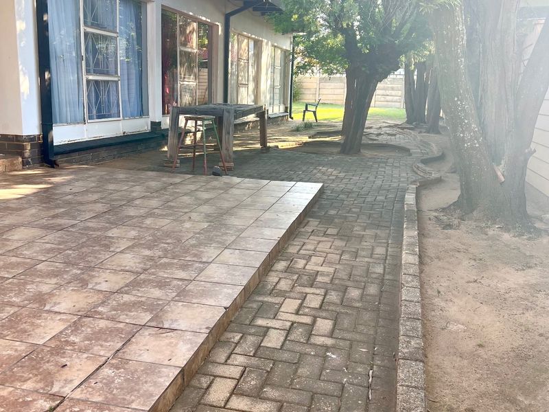 Rear exterior view featuring a tiled patio area, paved walkways, and mature trees along the side of the house.