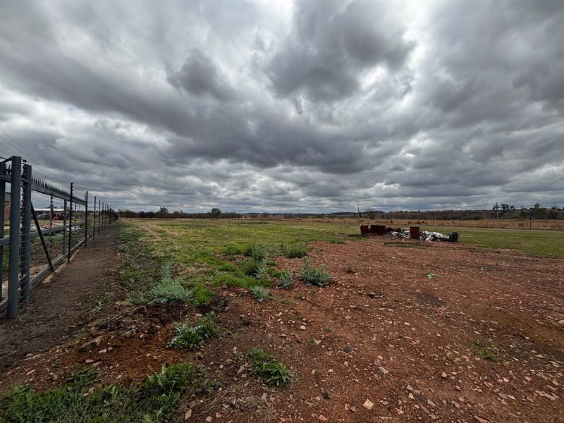 Expansive undeveloped industrial land featuring perimeter electric fencing and open terrain under a cloudy sky.