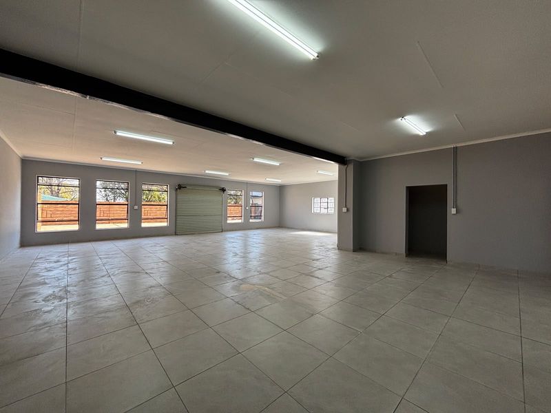 Spacious industrial utility area featuring tiled flooring, fluorescent lighting, and a roller shutter door, suitable for various commercial or storage applications.