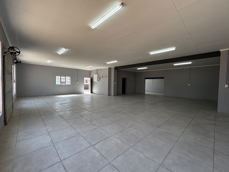 Spacious open-plan industrial unit featuring durable tiled flooring, bright fluorescent lighting, and a secure roller shutter door, ideal for versatile commercial use.