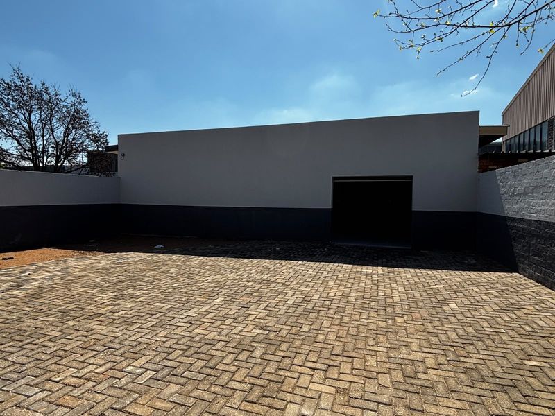 A paved rear courtyard area featuring a boundary wall and access to a garage space.