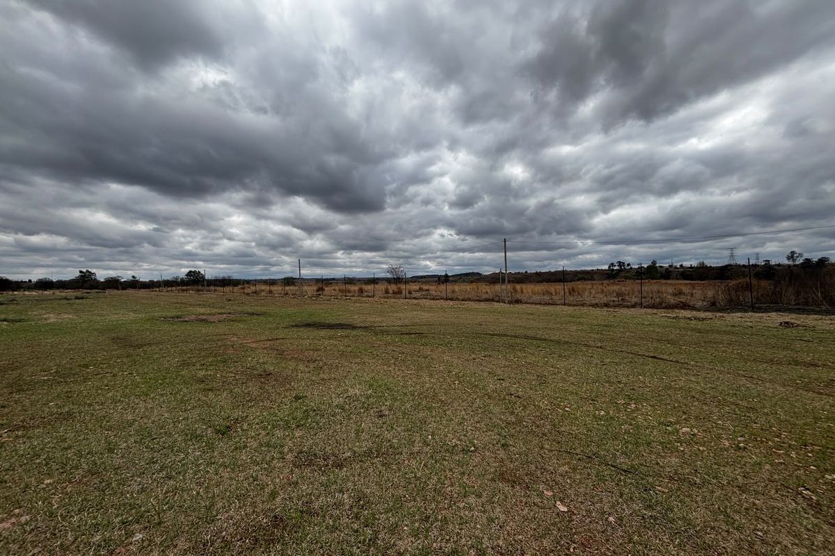 A wide, open industrial plot featuring a grass lawn and perimeter wire fencing under an overcast sky.