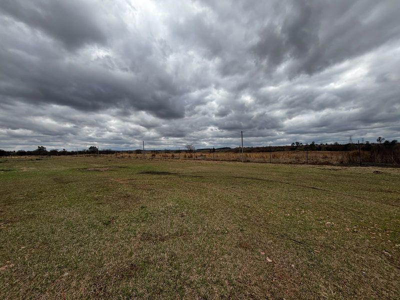 A wide, open industrial plot featuring a grass lawn and perimeter wire fencing under an overcast sky.