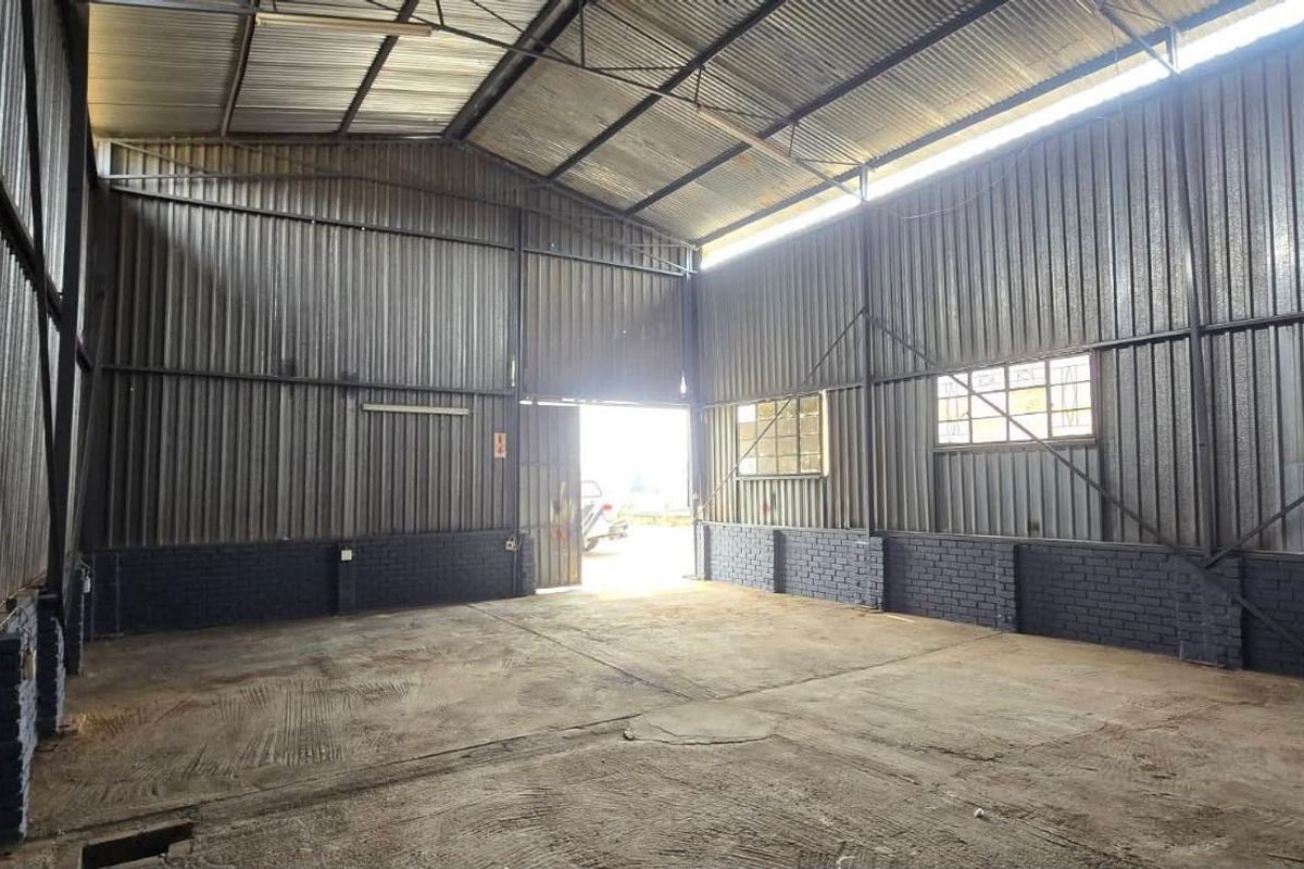 Spacious industrial utility area featuring corrugated metal walls, exposed steel roof trusses, and durable concrete flooring, suitable for workshop or storage use.