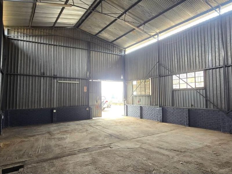 Spacious industrial utility area featuring corrugated metal walls, exposed steel roof trusses, and durable concrete flooring, suitable for workshop or storage use.