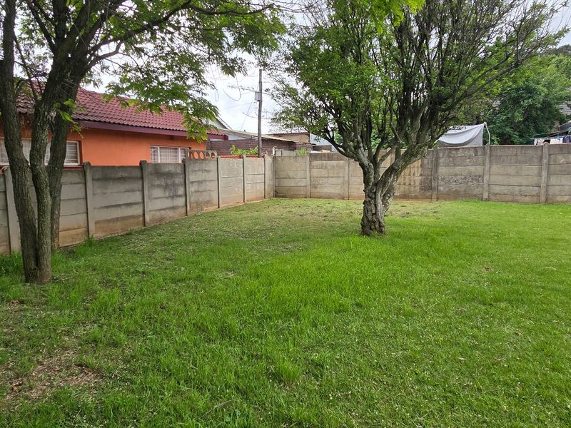 A spacious backyard featuring a well-established lawn, mature trees, and secure precast concrete boundary walls.