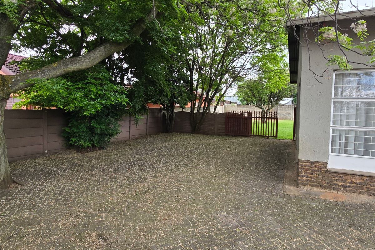 A paved rear courtyard area featuring a mature tree, precast boundary walling, and direct access to the main dwelling via a security-gated side entrance.