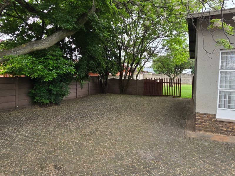 A paved rear courtyard area featuring a mature tree, precast boundary walling, and direct access to the main dwelling via a security-gated side entrance.