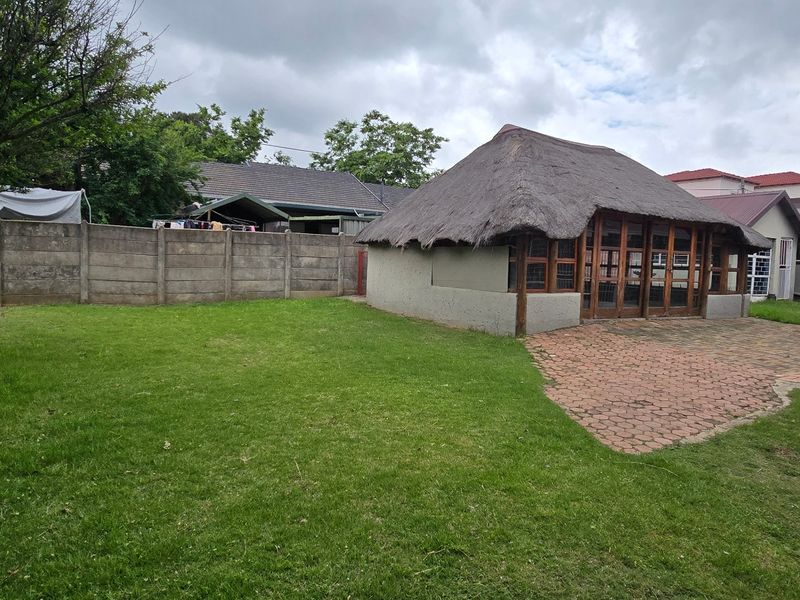 Spacious rear garden featuring a thatched roof lapa, paved patio area, and established lawn enclosed by a precast concrete boundary wall.