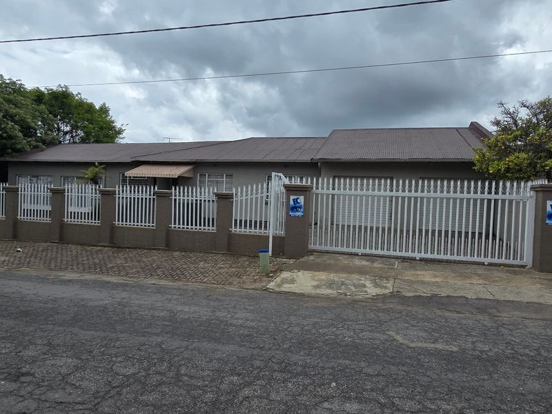 Front exterior view of a single-story house featuring a secure metal perimeter fence, sliding gate, and paved driveway access.