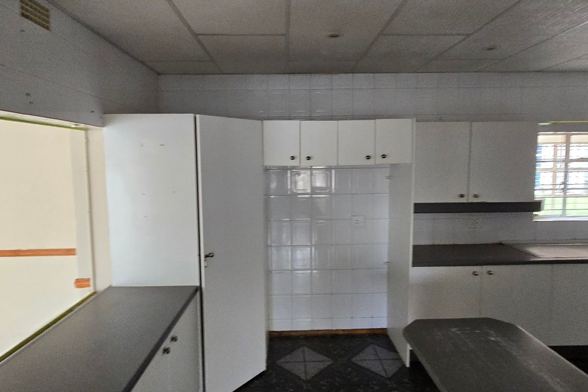 A dated, empty kitchen featuring white built-in cabinetry, dark laminate countertops, a stainless steel sink, and tiled flooring, offering potential for modernization.