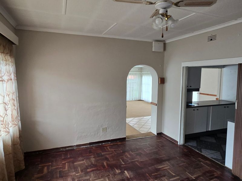 Spacious living area featuring classic parquet flooring, a ceiling fan, and an arched entryway leading to an adjacent room.