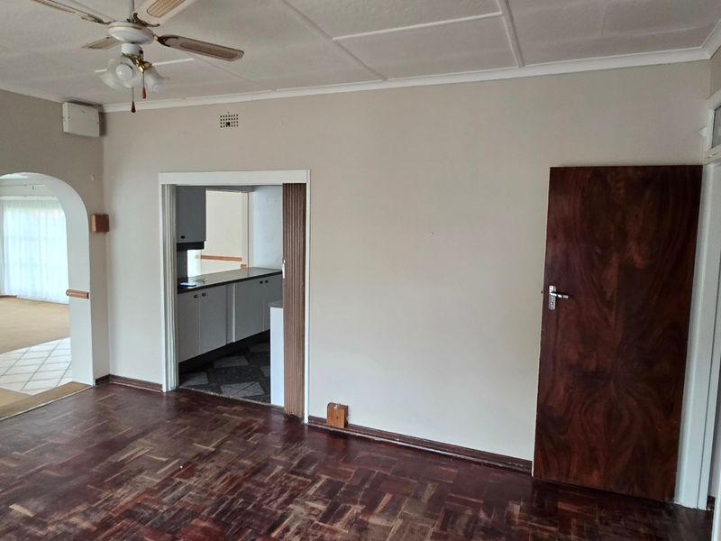 Spacious living area featuring classic parquet flooring, a ceiling fan, and an arched entryway leading to an adjacent room.