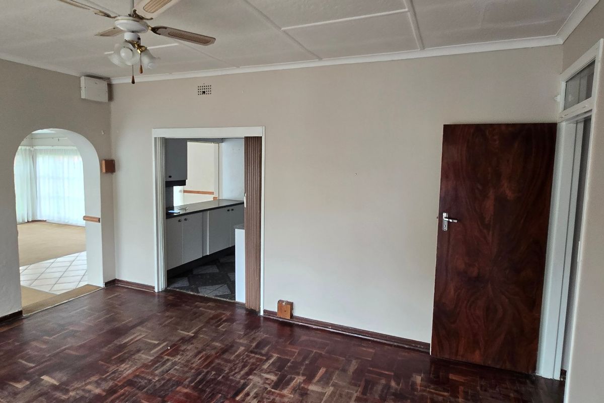 Spacious living area featuring classic parquet flooring, a ceiling fan, and an arched entryway leading to an adjacent room.