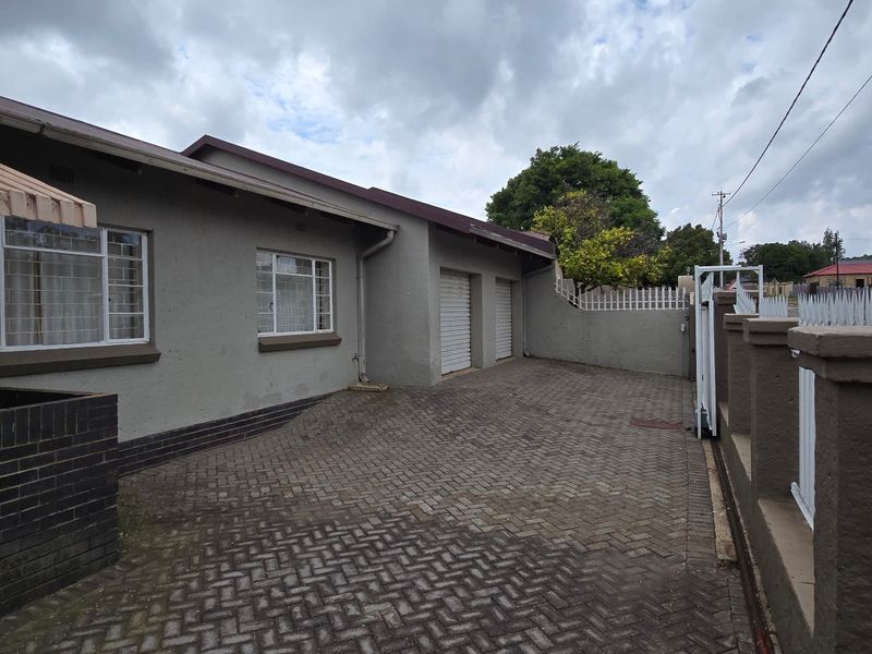 Front exterior view of the property featuring a paved driveway, double garage, and secure boundary wall with metal fencing.