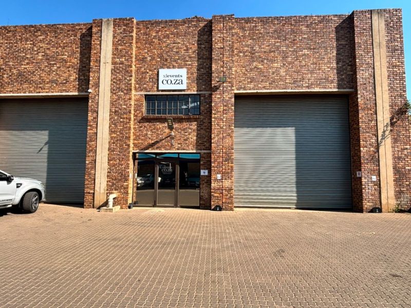 Industrial warehouse exterior featuring a face brick facade, two large roller shutter doors, and a paved driveway entrance.