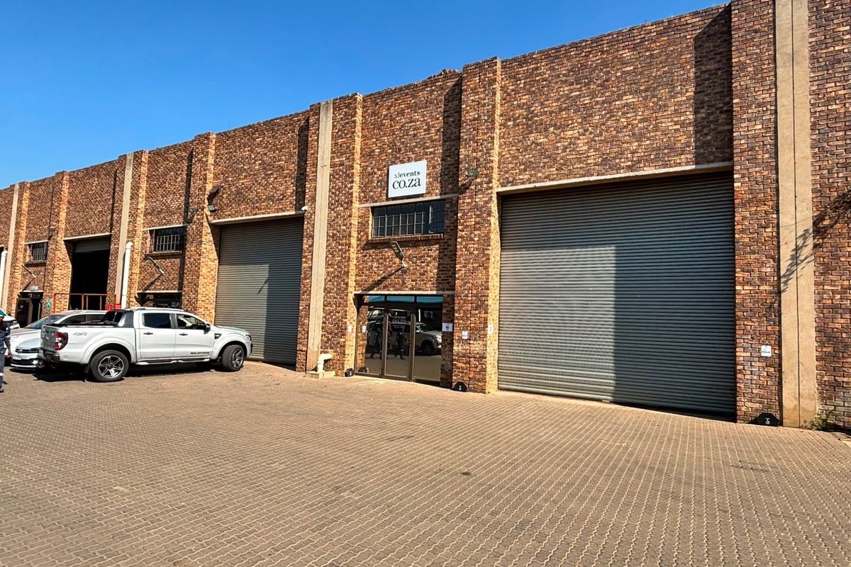 Industrial warehouse unit featuring a face brick facade, multiple roller shutter doors, and a paved driveway entrance.