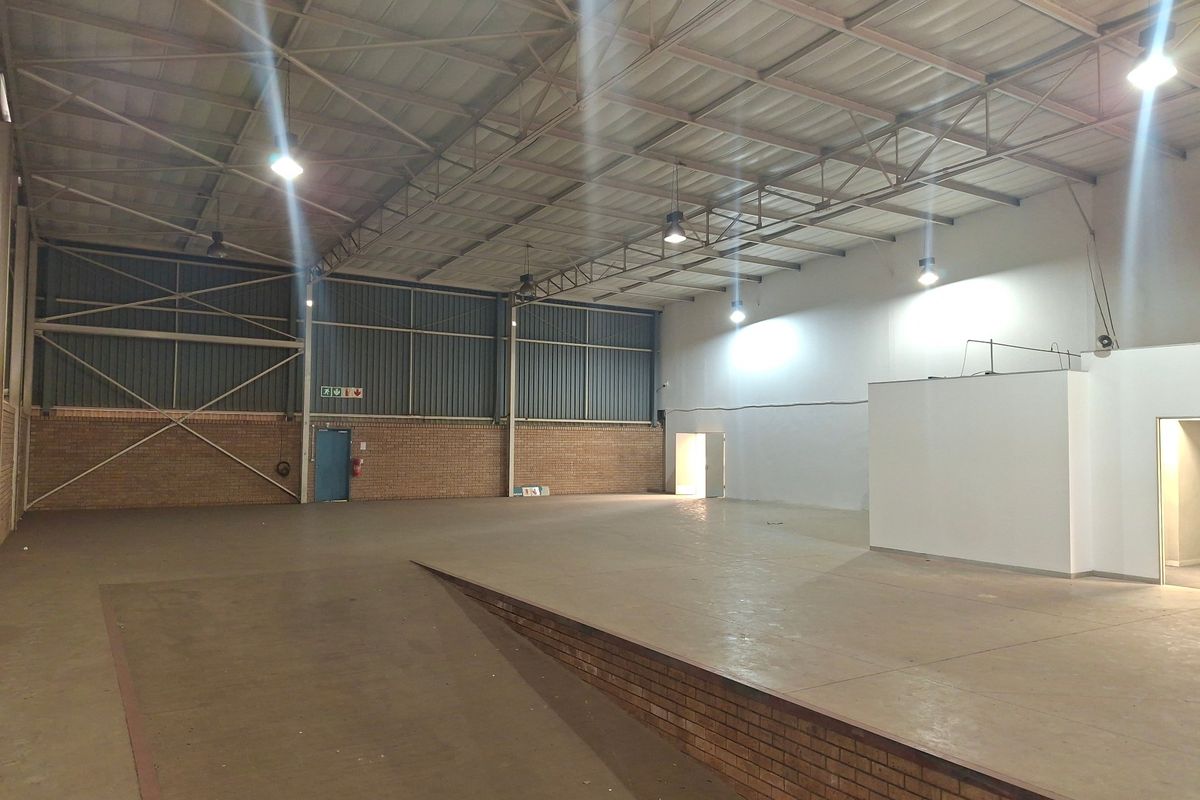 Spacious industrial warehouse unit featuring high-bay lighting, exposed steel roof trusses, and a raised concrete platform, suitable for various commercial or storage applications.