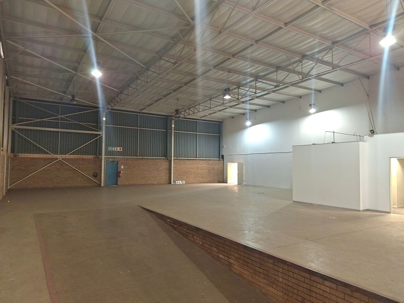 Spacious industrial warehouse unit featuring high-bay lighting, exposed steel roof trusses, and a raised concrete platform, suitable for various commercial or storage applications.