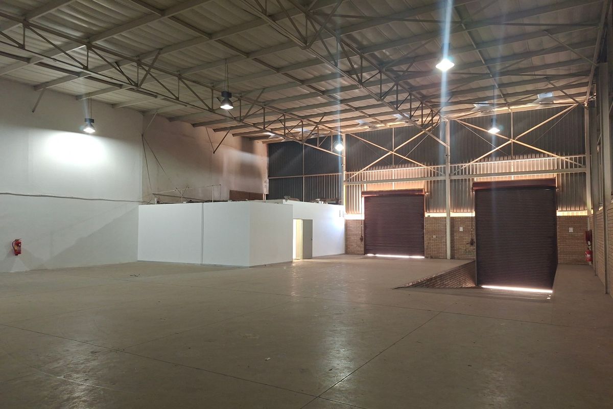 Spacious industrial warehouse featuring high ceilings with exposed steel trusses, concrete flooring, multiple roller shutter doors, and a dedicated loading pit.
