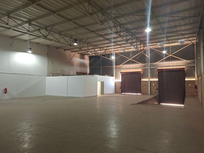 Spacious industrial warehouse featuring high ceilings with exposed steel trusses, concrete flooring, multiple roller shutter doors, and a dedicated loading pit.