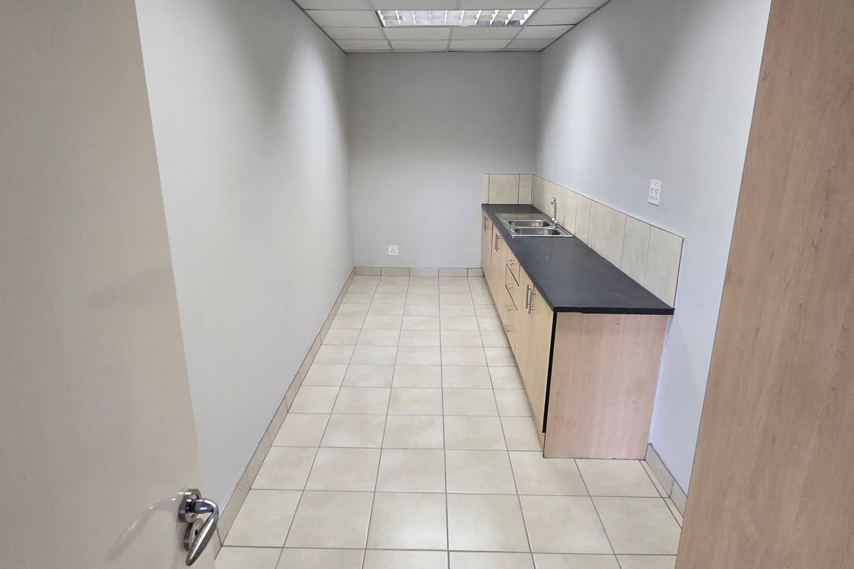 A functional, empty kitchenette featuring built-in cabinetry, a laminate countertop, and a stainless steel sink, suitable for office or commercial use.