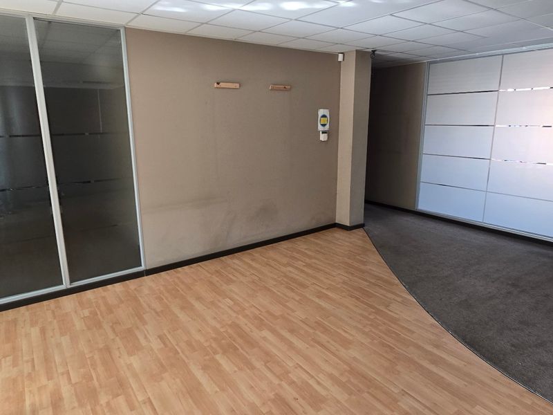 An empty commercial office space featuring glass partitions, a mix of laminate and carpet flooring, and a suspended ceiling.