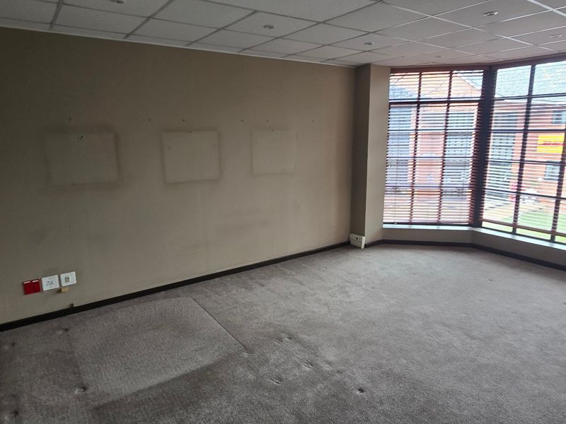 An empty commercial office space featuring large bay windows with fitted blinds, suspended ceiling, and carpeted flooring, suitable for a professional workspace.
