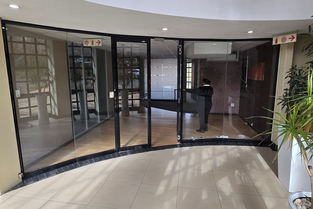 A bright and modern commercial entrance lobby featuring glass partitions, tiled flooring, and recessed lighting, providing a professional and welcoming reception area.