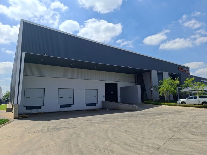 Modern industrial warehouse facility featuring multiple roller shutter loading doors, a concrete hardstand area, and professional metal cladding exterior.