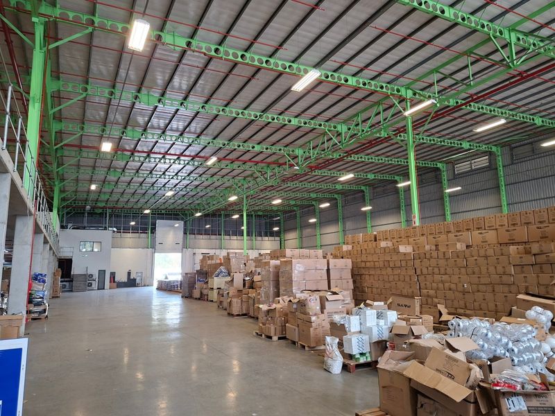 Spacious industrial warehouse featuring high ceilings with exposed steel trusses, concrete flooring, and a mezzanine level, suitable for storage or manufacturing operations.