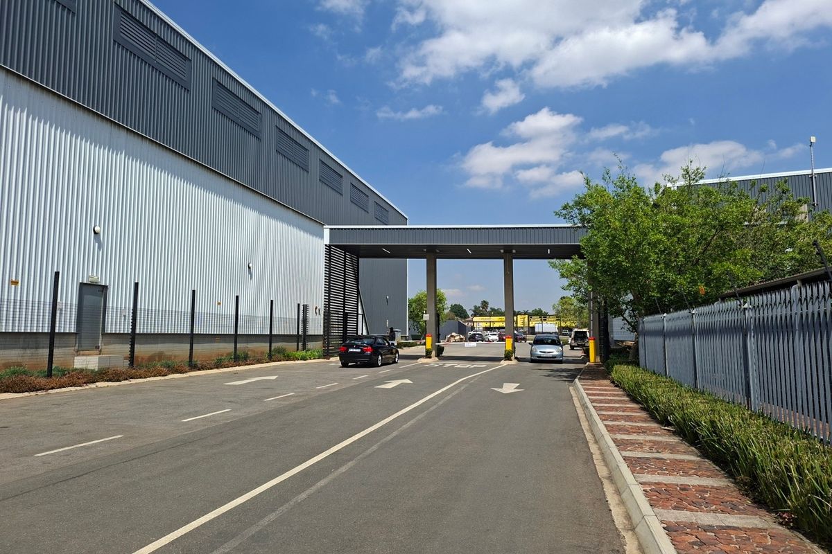 Industrial property entrance featuring a secure gated access point, metal clad warehouse facade, and paved driveway with perimeter security fencing.