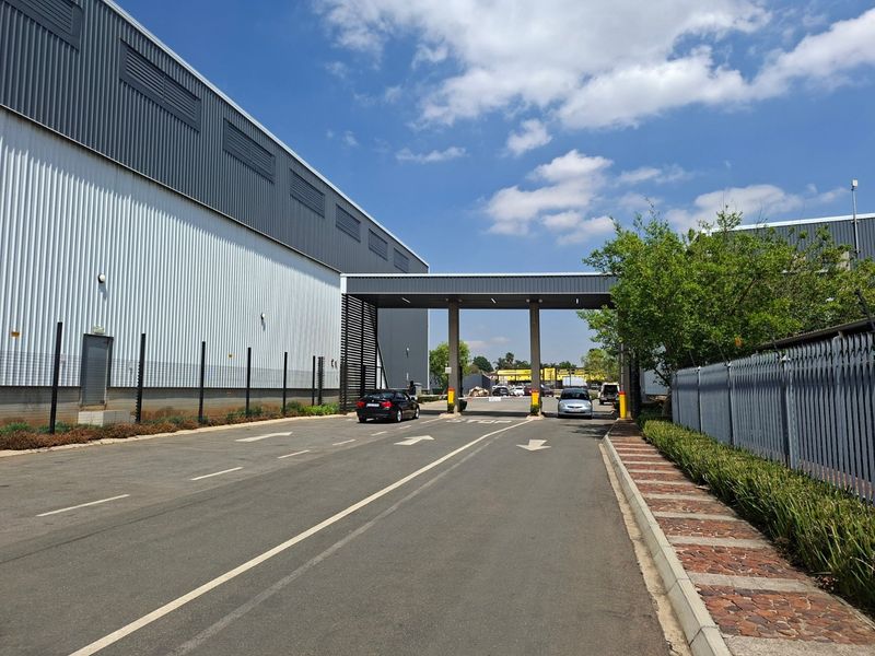 Industrial property entrance featuring a secure gated access point, metal clad warehouse facade, and paved driveway with perimeter security fencing.