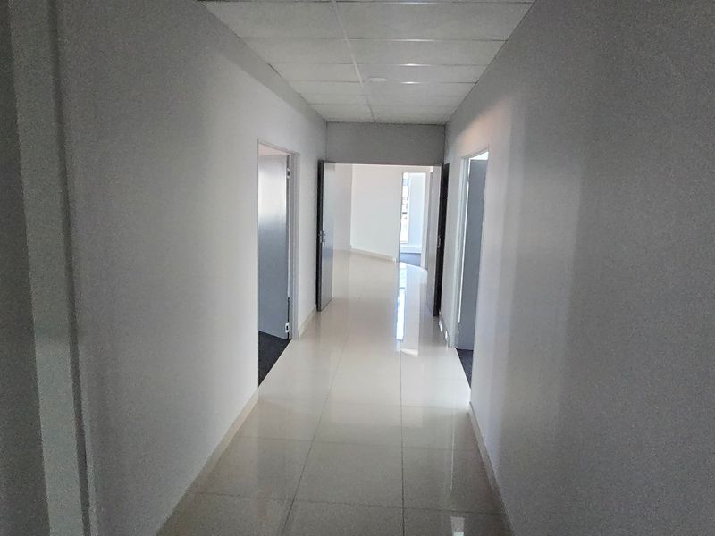 A clean, empty commercial hallway featuring tiled flooring and a suspended ceiling, providing access to multiple office or utility rooms.