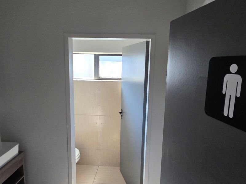 A clean, modern commercial restroom featuring a wall-mounted basin with vanity storage and a separate tiled toilet cubicle.