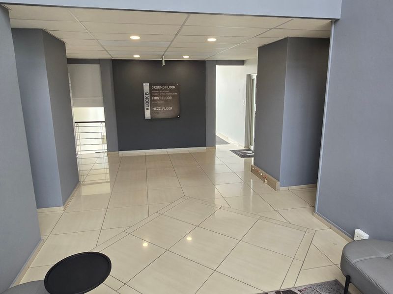 A clean and modern commercial building entrance lobby featuring tiled flooring, recessed lighting, and clear directional signage for building levels.