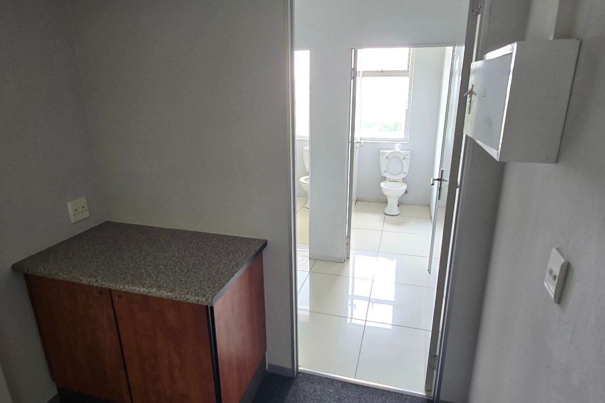 A functional commercial utility area featuring built-in cabinetry and a fire extinguisher, leading into a tiled restroom facility with a toilet.