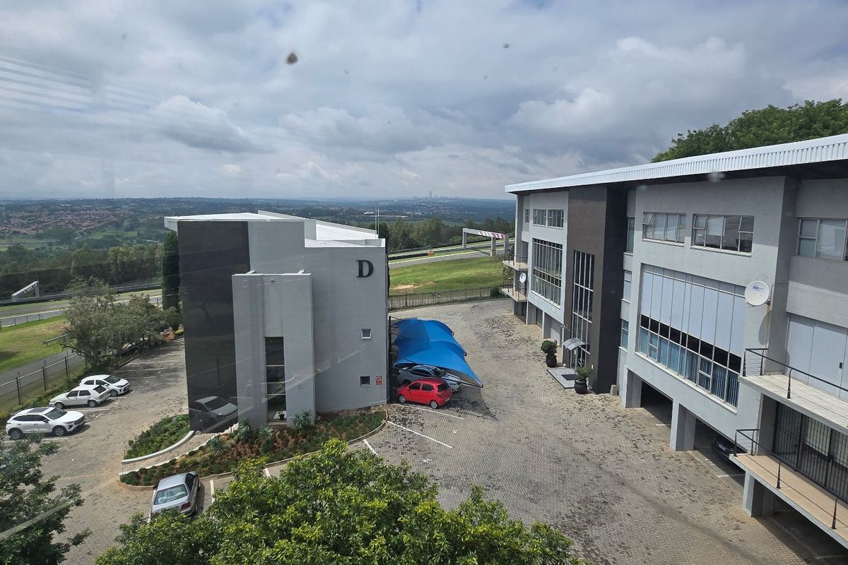 Aerial view of a commercial office park featuring multi-story buildings, paved parking areas with shade cloth carports, and surrounding landscape.