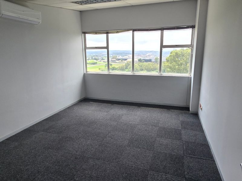 A clean, empty office space featuring carpet tiles, a suspended ceiling, split-system air conditioning, and large windows with scenic views.