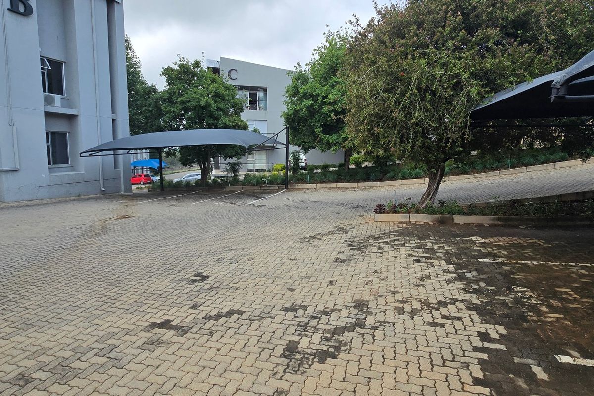 Exterior view of a commercial property featuring a paved parking area with shade cloth carports and access to building blocks.