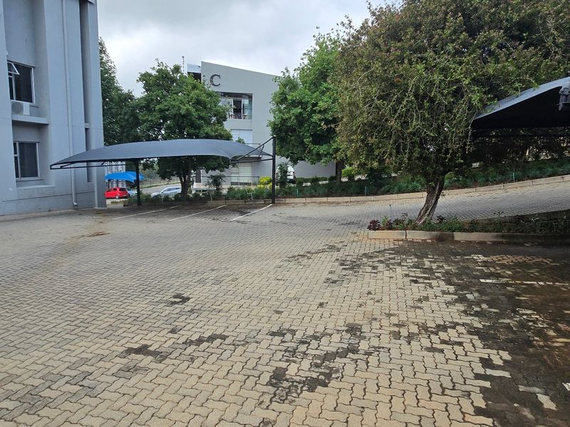 Exterior view of a commercial property featuring a paved parking area with shade cloth carports and access to building blocks.
