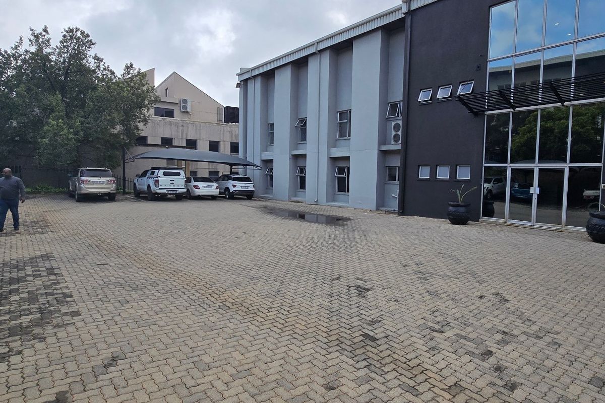 Commercial property exterior featuring a paved parking area with carport structures and a modern glass facade entrance.
