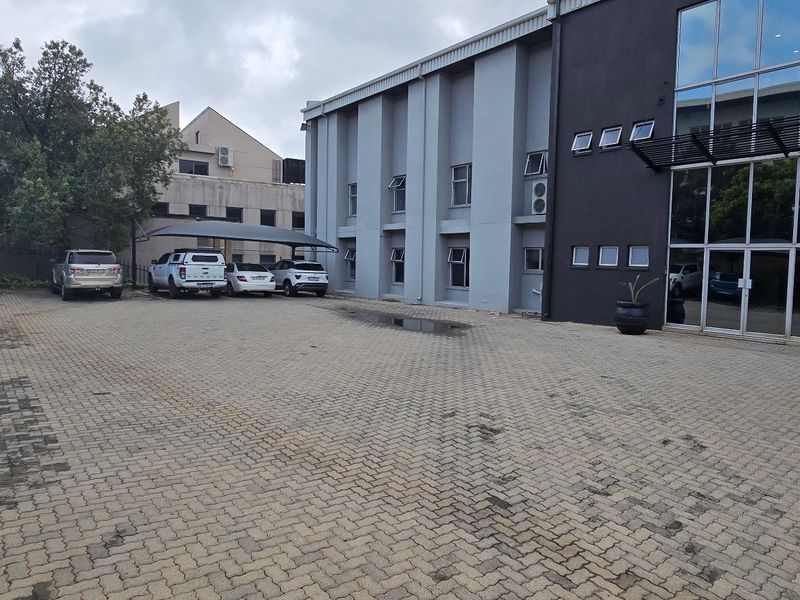 Commercial property exterior featuring a paved parking area with carport structures and a modern glass facade entrance.