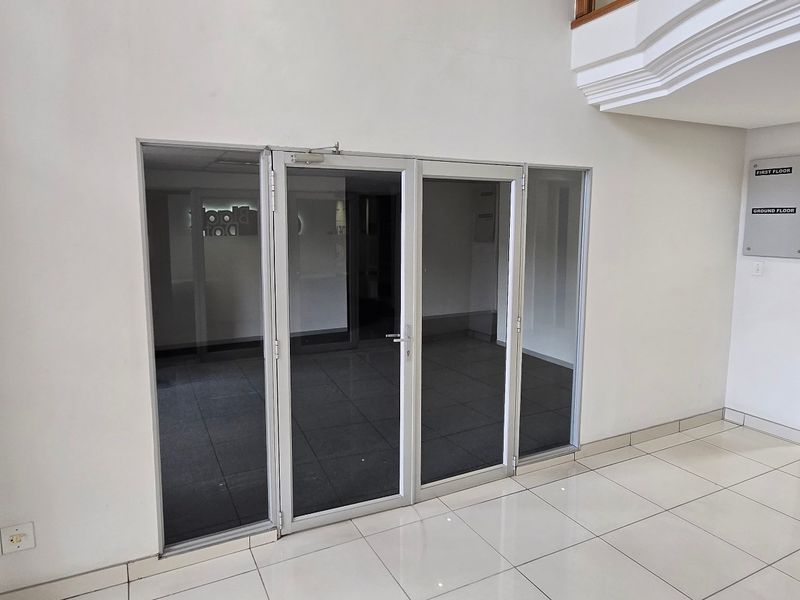 A bright commercial entrance lobby featuring tiled flooring, aluminium glass doors, and a staircase leading to the upper level.